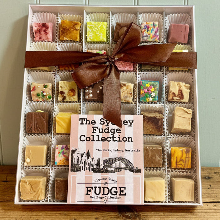A boxed assortment of fudge pieces labeled 'The Sydney Fudge Collection' in a white tray, tied with a brown ribbon, photographed on a retail counter.